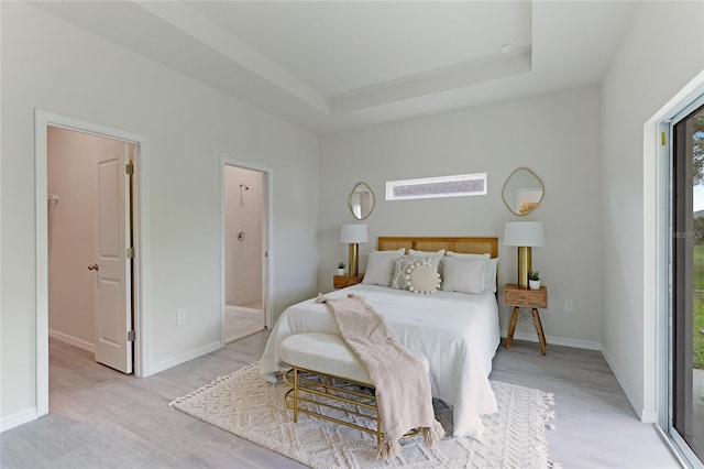 bedroom featuring a raised ceiling, connected bathroom, access to outside, and light hardwood / wood-style flooring