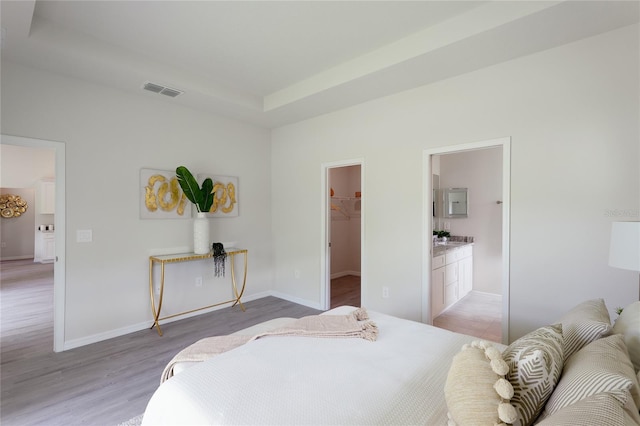 bedroom with light wood-type flooring, connected bathroom, a spacious closet, and a closet