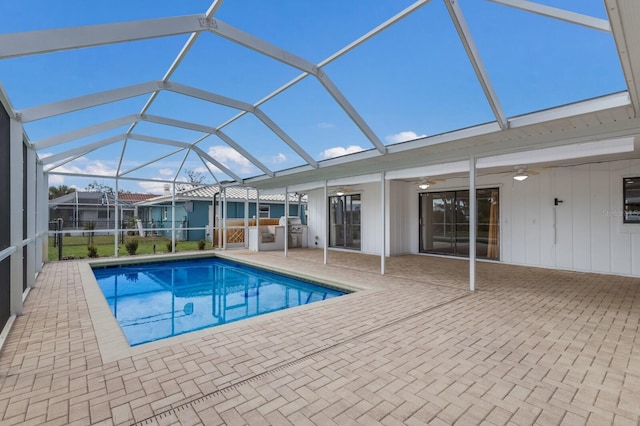 view of swimming pool featuring glass enclosure, a patio area, a grill, an outdoor kitchen, and ceiling fan