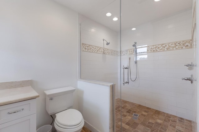 bathroom featuring toilet, tiled shower, and vanity