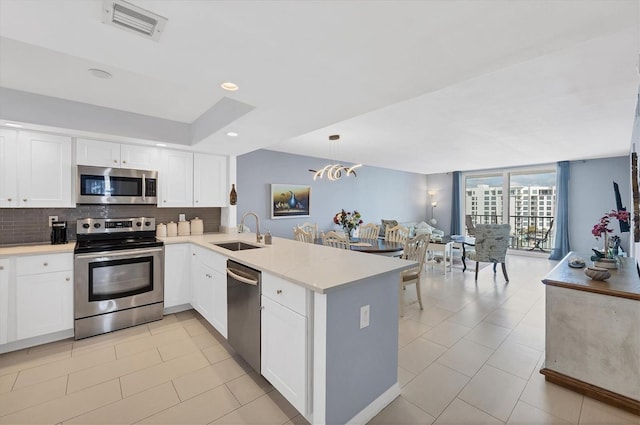 kitchen with kitchen peninsula, tasteful backsplash, stainless steel appliances, sink, and hanging light fixtures