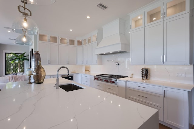 kitchen with sink, stainless steel gas cooktop, light stone counters, premium range hood, and white cabinets