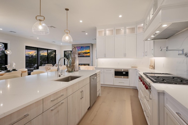 kitchen with custom exhaust hood, stainless steel appliances, sink, white cabinets, and hanging light fixtures