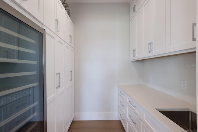 kitchen featuring sink, hardwood / wood-style flooring, white cabinetry, and light stone counters