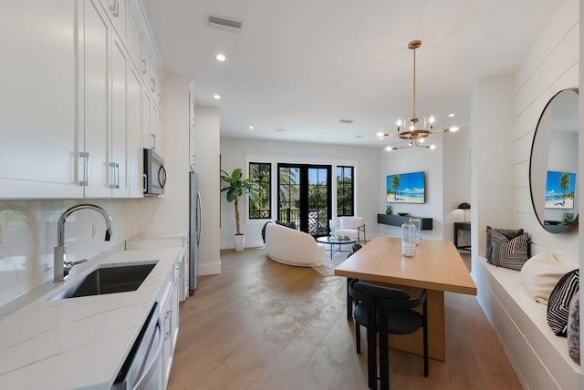 dining room featuring french doors, light wood-type flooring, an inviting chandelier, and sink