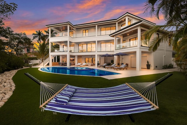 back house at dusk with a balcony, a patio, and a pool with hot tub