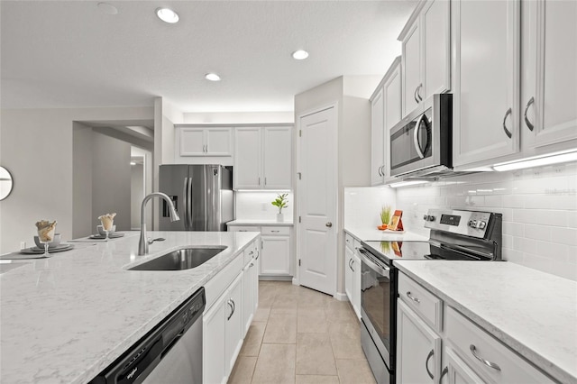 kitchen featuring tasteful backsplash, light stone counters, stainless steel appliances, sink, and light tile patterned floors