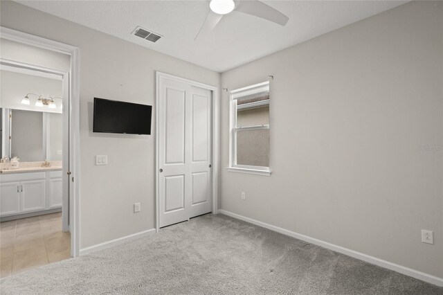 unfurnished bedroom featuring ensuite bathroom, ceiling fan, light colored carpet, and a closet