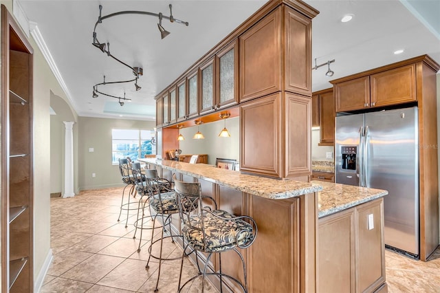 kitchen with a breakfast bar, crown molding, light stone counters, decorative light fixtures, and stainless steel fridge