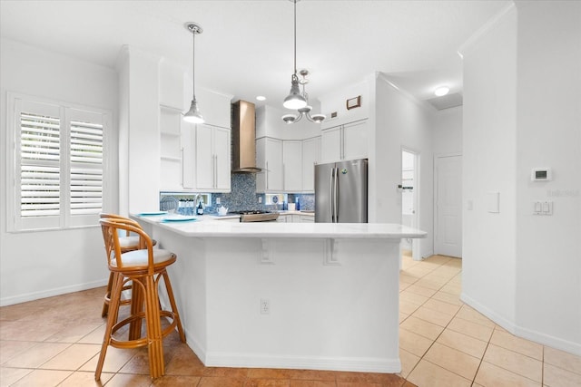 kitchen featuring wall chimney exhaust hood, stainless steel appliances, pendant lighting, white cabinets, and a breakfast bar area