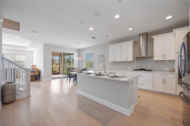 kitchen featuring white cabinets, an island with sink, wall chimney exhaust hood, and stainless steel appliances