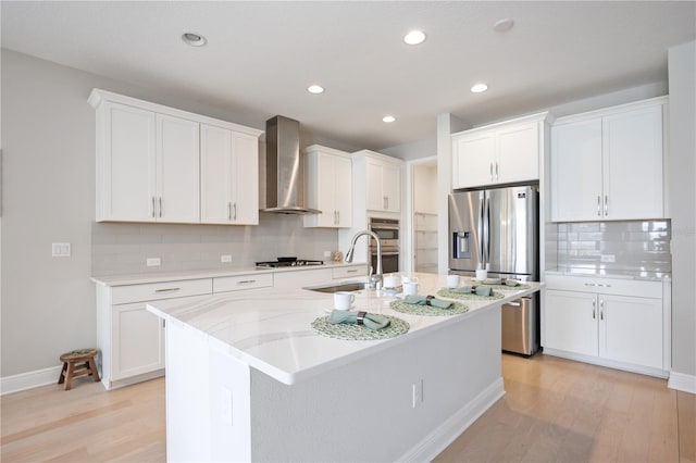 kitchen with sink, a center island with sink, white cabinetry, and wall chimney range hood