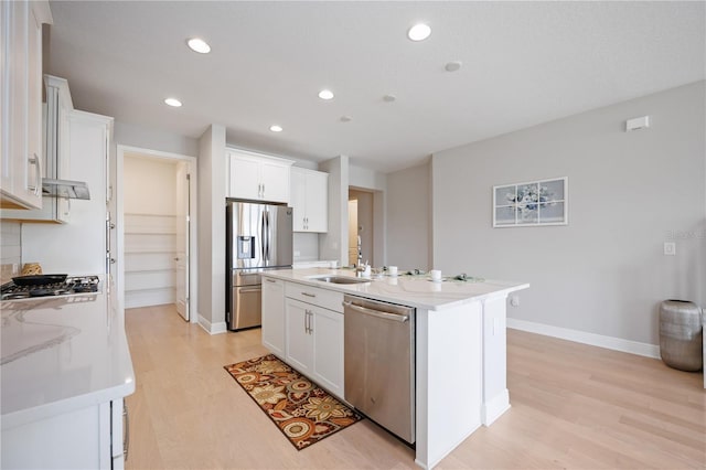 kitchen with white cabinets, stainless steel appliances, a kitchen island with sink, and light hardwood / wood-style floors