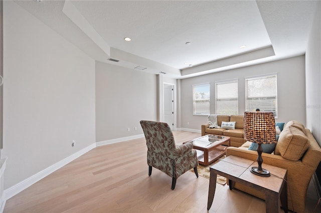 living room with light hardwood / wood-style flooring and a tray ceiling