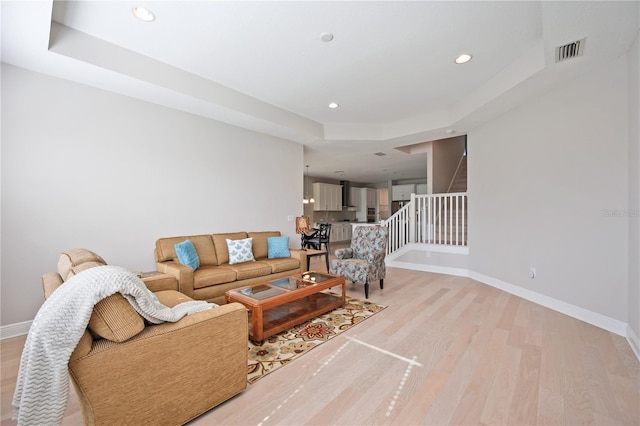 living room with light wood-type flooring and a raised ceiling