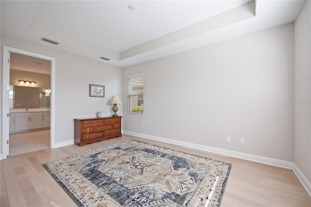 bedroom featuring a raised ceiling, connected bathroom, and light hardwood / wood-style flooring