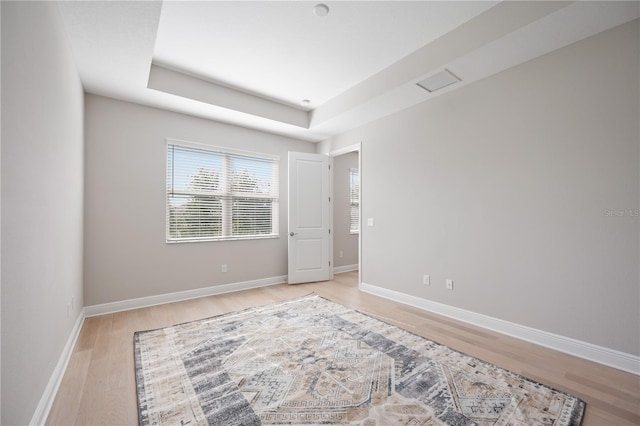 spare room featuring a tray ceiling and light hardwood / wood-style floors