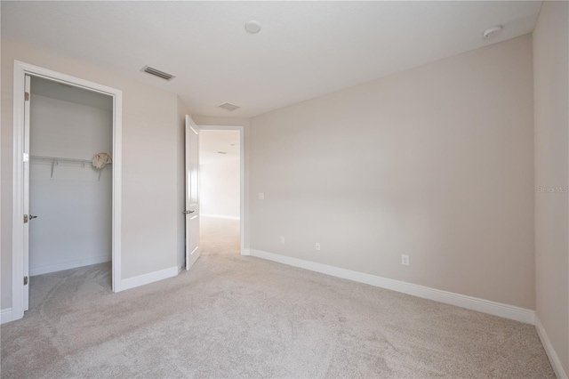 unfurnished bedroom featuring a spacious closet, a closet, and light carpet