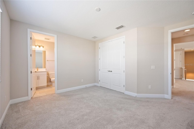 unfurnished bedroom featuring ensuite bathroom, a closet, light carpet, and sink