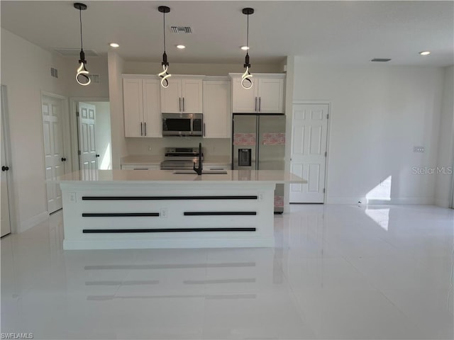 kitchen featuring appliances with stainless steel finishes, an island with sink, white cabinets, decorative light fixtures, and sink