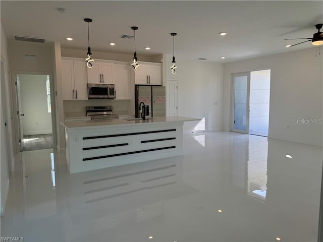 kitchen featuring stainless steel appliances, an island with sink, white cabinets, decorative light fixtures, and sink