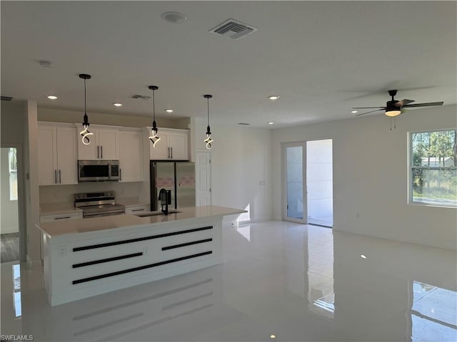 kitchen with stainless steel appliances, sink, white cabinetry, an island with sink, and pendant lighting