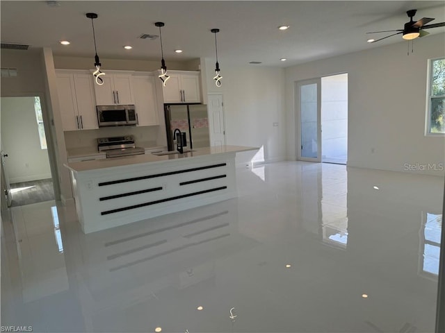 kitchen with stainless steel appliances, white cabinetry, hanging light fixtures, and an island with sink