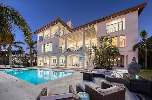 rear view of property with a patio area, a balcony, and an outdoor living space with a fire pit