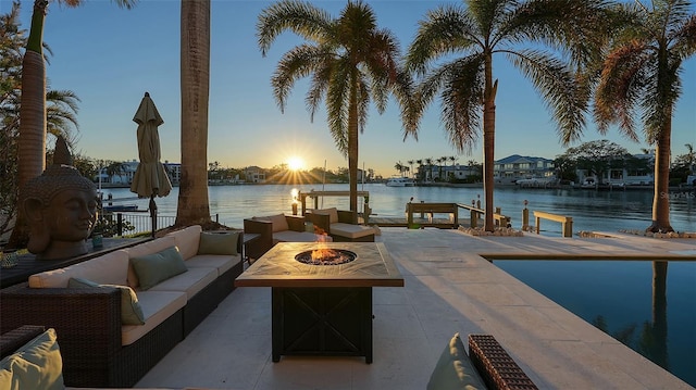 patio terrace at dusk featuring a water view and an outdoor living space with a fire pit