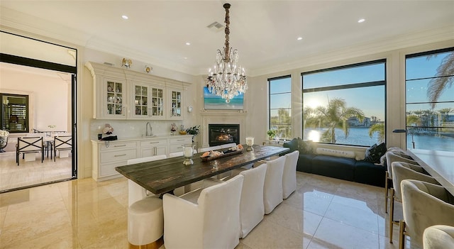 dining space featuring crown molding, sink, light tile patterned floors, a water view, and a chandelier