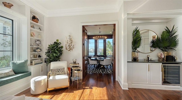 sitting room featuring ornamental molding, beverage cooler, built in features, a notable chandelier, and dark hardwood / wood-style floors