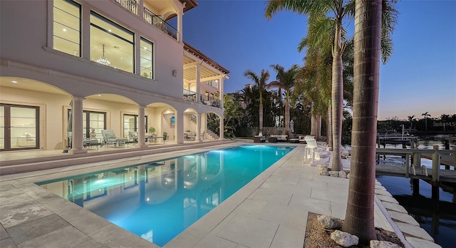 pool at dusk featuring a boat dock and a patio