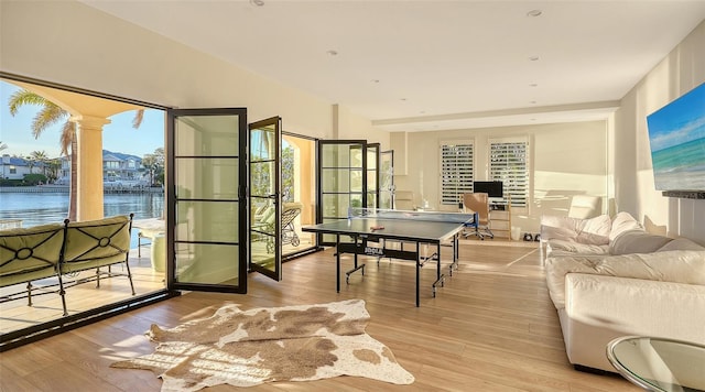 recreation room featuring light wood-type flooring, a water view, and decorative columns