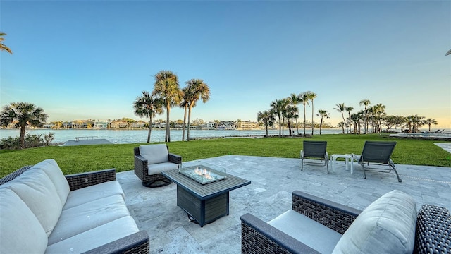 patio terrace at dusk with an outdoor living space with a fire pit, a lawn, and a water view