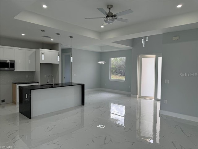 kitchen with pendant lighting, white cabinetry, an island with sink, and a tray ceiling