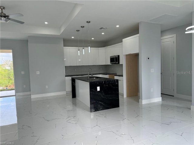 kitchen featuring hanging light fixtures, a kitchen island with sink, backsplash, white cabinetry, and sink