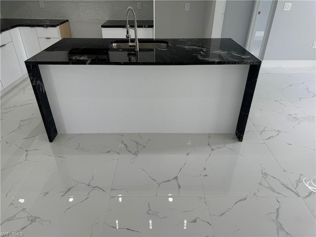 kitchen with dark stone countertops, a center island with sink, decorative backsplash, white cabinets, and sink