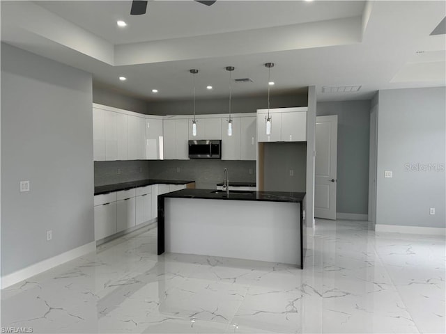 kitchen featuring sink, decorative light fixtures, white cabinets, decorative backsplash, and a kitchen island with sink