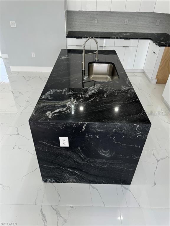 interior details featuring sink, white cabinetry, and dark stone countertops