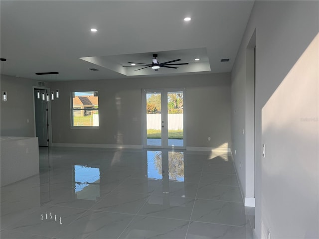 empty room with a tray ceiling, french doors, and ceiling fan