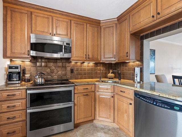 kitchen with decorative backsplash, light stone counters, sink, and appliances with stainless steel finishes