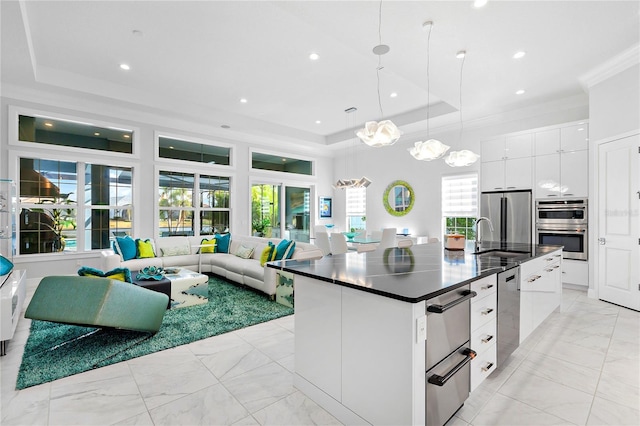 kitchen featuring decorative light fixtures, white cabinetry, a kitchen island with sink, and a tray ceiling