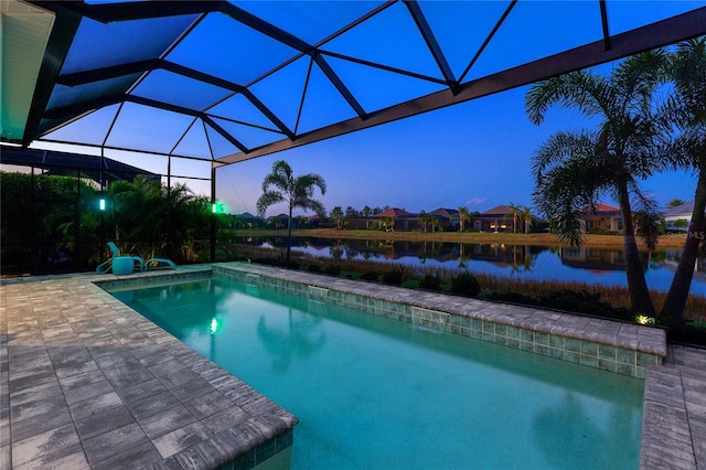 pool at dusk featuring glass enclosure, a patio area, and a water view