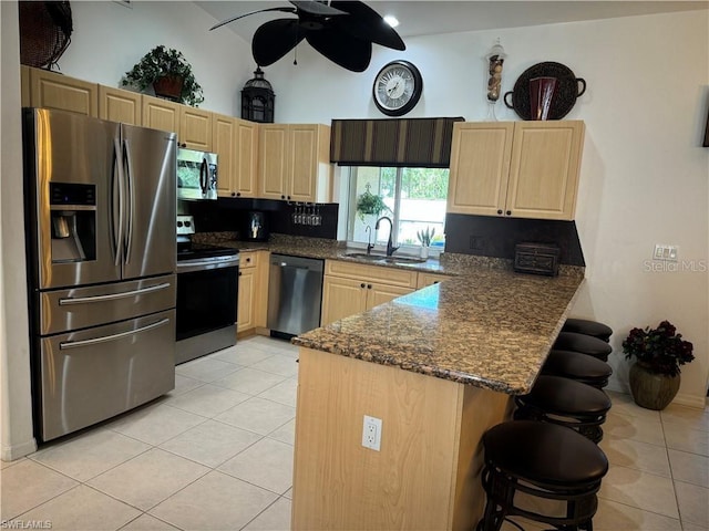 kitchen featuring kitchen peninsula, stainless steel appliances, dark stone counters, ceiling fan, and sink