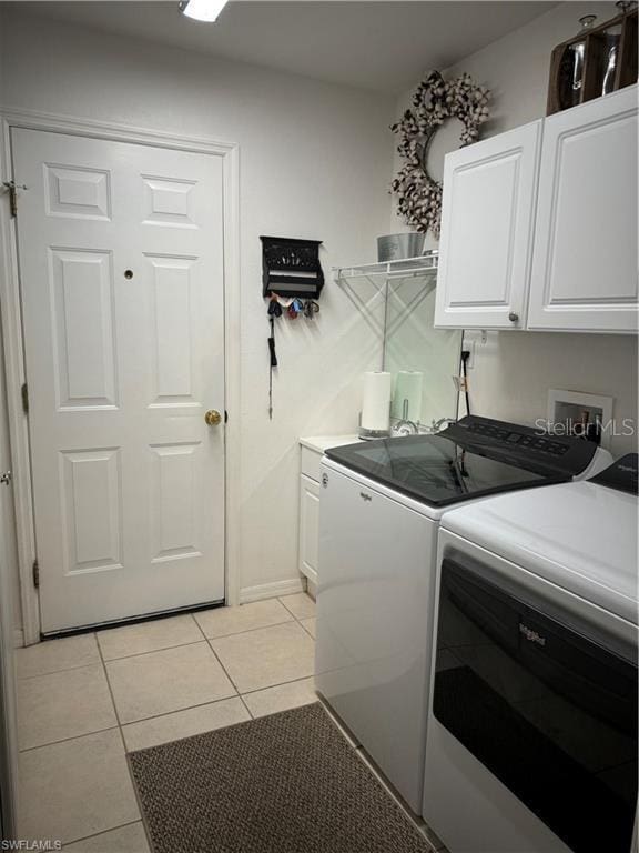 clothes washing area featuring washer and clothes dryer, light tile patterned floors, and cabinets