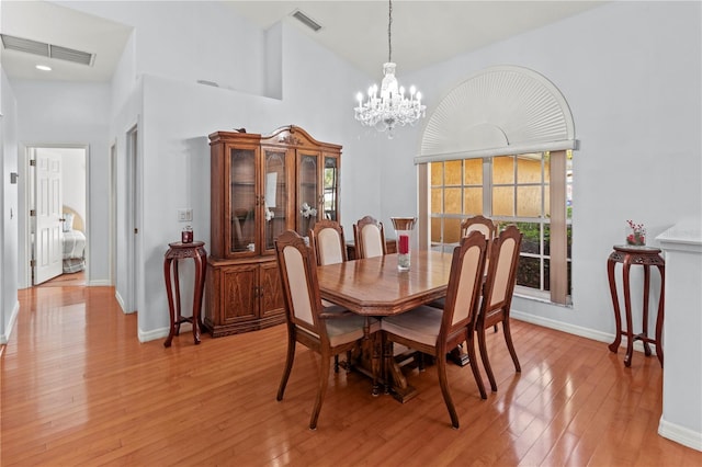 dining area with light wood-type flooring, high vaulted ceiling, and an inviting chandelier