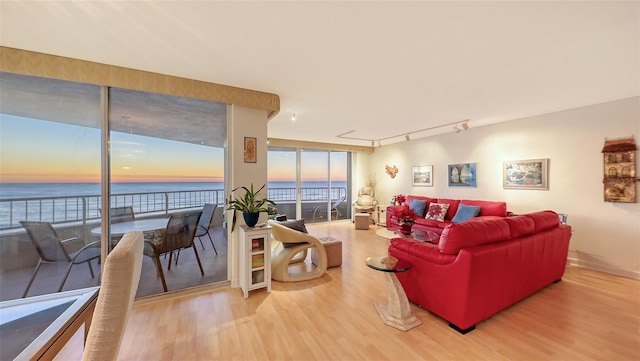 living room with floor to ceiling windows, hardwood / wood-style floors, a water view, and rail lighting