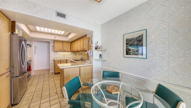 kitchen featuring kitchen peninsula, stainless steel fridge, light tile patterned floors, and sink