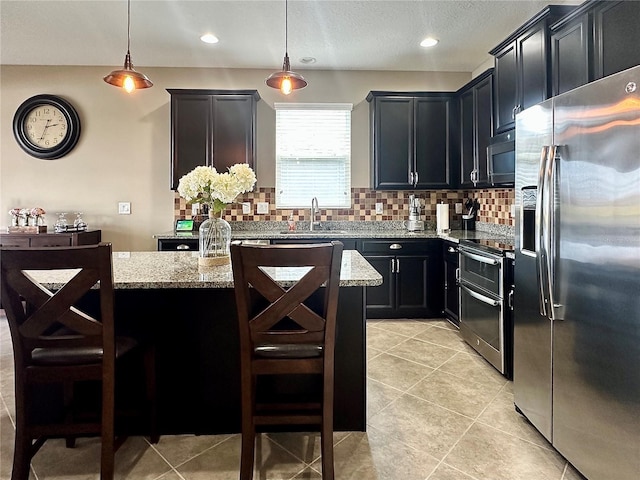 kitchen featuring decorative light fixtures, sink, a breakfast bar area, and appliances with stainless steel finishes