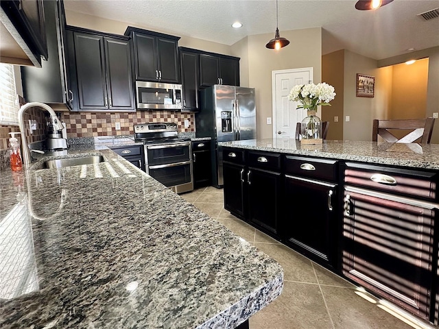 kitchen featuring light stone countertops, sink, hanging light fixtures, stainless steel appliances, and backsplash